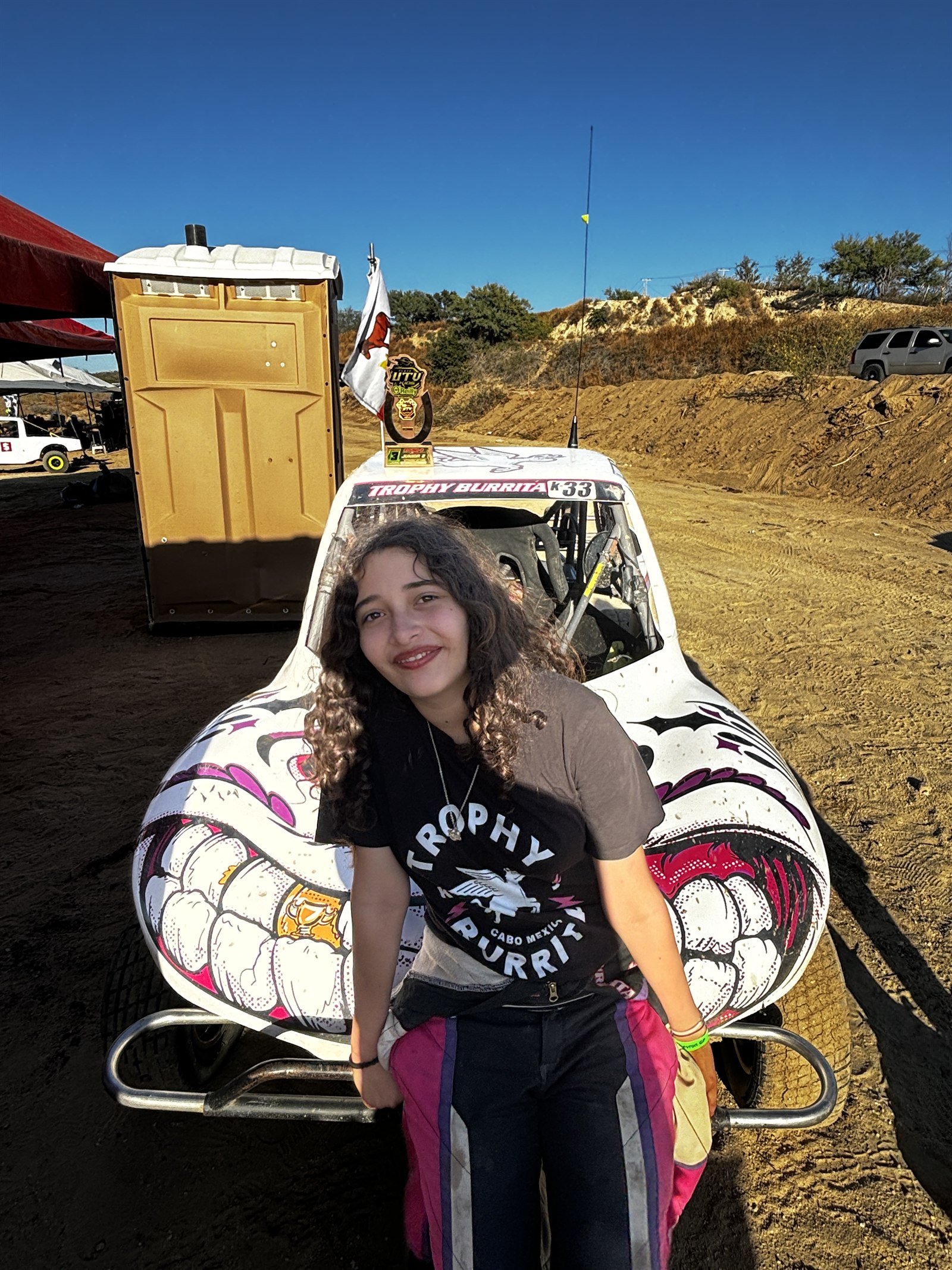 Emma Valentina Flynn smiling in front of the Trophy Burrita car at the track.